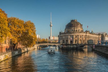 Berlin cityscape with museum island and the river Spree in autumn. a boat is sailing on the river. In the background the TV tower is visible in the blue sky on sunny day