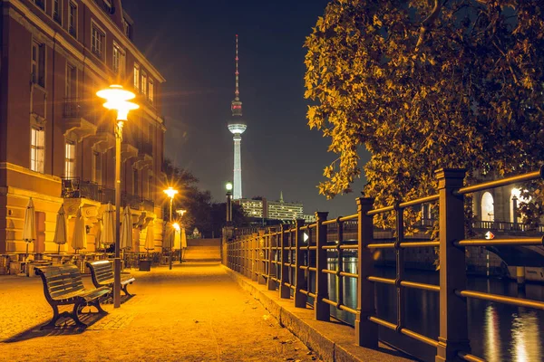Promenade on the Spree shore at night. Promenade near the museum island. In the background is the TV tower. There are benches on the way. The path is illuminated in autumn mood