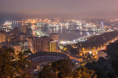 İspanyol şehir Malaga gece. Liman ve yapay ışık yukarıdan bir boğa yüzük ile eski şehir. Yapı ve gemi limanda görülebilir. Dönme dolap ve yolcu limanda gemi. Liman ve ağaçlar su yansıması