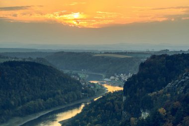 Günbatımı Elbe kumtaşı Dağları Sakson İsviçre Ulusal Parkı'nda. Ormanlar ve kaya oluşumu kıyısında Elbe ufukta bir köy