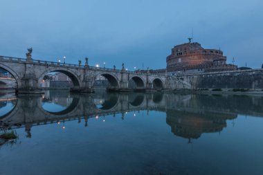 Sabah kale Sant Angelo ve mavi gökyüzü ile suları üzerinde Aurelius köprü ile Tiber Nehri. Kıyıdaki ışıklı binaların ve ağaçların suyundaki yansımalar