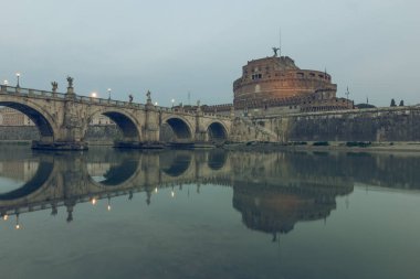 Nehir Tiber, Roma'nın tarihi merkezinde, sular üzerindeki Aurelius köprüsü ve sant angelo kalesi ile alacakaranlıkta. Işıklı binalar ile sudaki taş köprünün yansımaları
