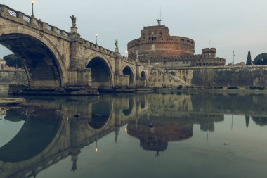 Nehir Tiber, Roma'nın tarihi merkezinde, sular üzerindeki Aurelius köprüsü ile gün batımında sant angelo kalesi ile birlikte bulutlar. Işıklı binalar ile sudaki taş köprünün yansımaları