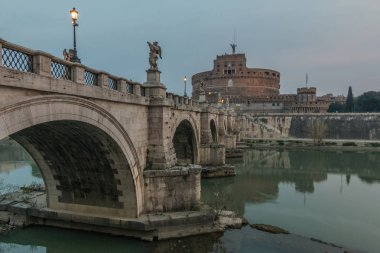 Şafakta Tiber üzerinde aydınlatma ile Aurelius köprü. Taş köprünün arka planında, Roma'nın eski kentinin merkezinde yer alan Sant Angelo Kalesi yer almaktadır. gökyüzünde bulutlar