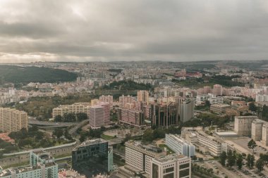 Yukarıdan Portekiz'in başkenti Lizbon. Gökyüzünde bulutlar ve ön planda stadyum ile şehir silueti. Ufukta manzara ve gemiler ile nehir adı Tejo binalar ve ağız