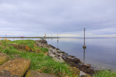 Sabahları Reykjavik yakınlarındaki Grotta adası ile Atlantik Okyanusu'nda taş sahil ve bulutlar gökyüzünde. arka planda ıssız deniz feneri ve İzlanda evleri. Kuş mabedi yarımadası