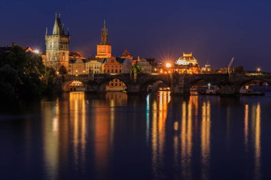 Prag'da Charles Köprüsü ile geceleyin. Vltava üzerinde panoramik görünümü. Eski Şehir kulesi ve eski şehir ve Küçük Şehir ve su yansımaları arasında aydınlatma ile tarihi taş köprü