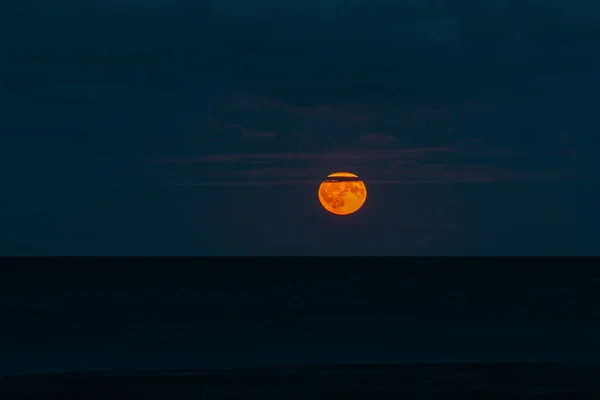 Moonrise on the Baltic Sea. Moon over the water surface with a dark blue sky. Yellow colored moon on the horizon with smooth water surface and few clouds