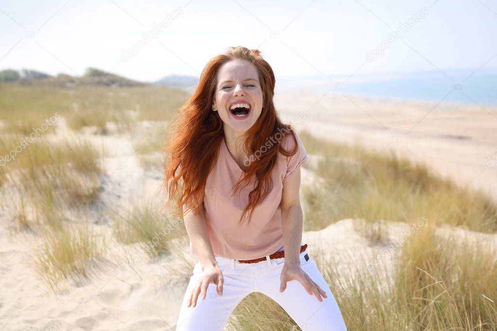 Beautiful redhead woman standing at the beach laughing