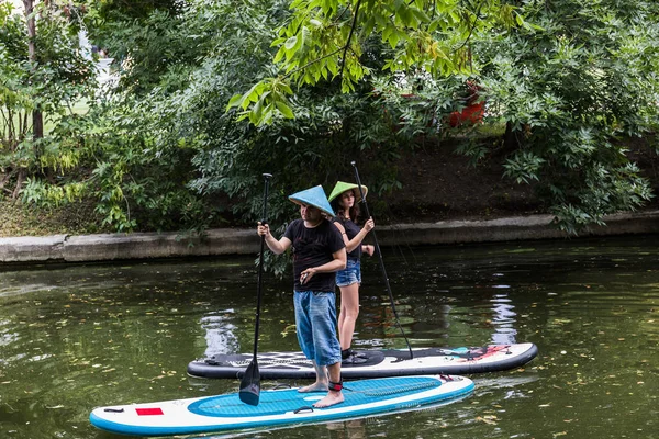 Moskova, Park Krasnaya Presnya, 05 Temmuz 2018: bir genç kız ve adam ile bir yandan çarklı ve hasır şapkalı duruyor bir gölet üzerinde sörf tahtası üzerinde. Moskova, Park üzerinde Krasnaya Presnya-Temmuz 05, 2018: