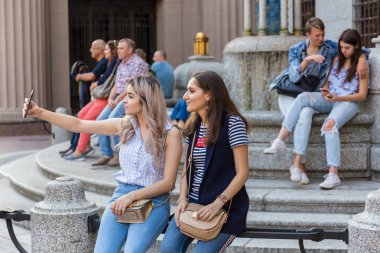 Moskova, Arbat Sokağı, 8 Eylül 2018: bir bankta oturan ve bir smartphone kullanarak fotoğrafı iki genç kız