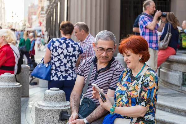 Moskova, Arbat Sokağı, 8 Eylül 2018: A Olgun çift bir bankta oturur ve smartphone birlikte saatler.