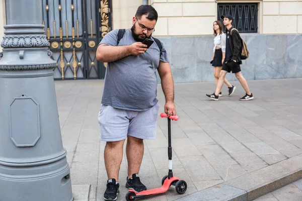 Moskova, Tverskaya street, 8 Eylül 2018: şişko gri t-shirt ve şort smartphone ve bir çocuk scooter tutan genç adam