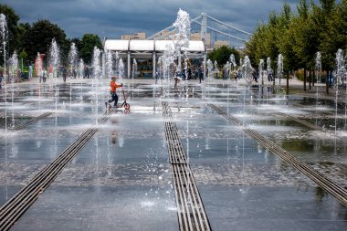 Su fıskiyelerinin arasında scooter süren küçük bir çocuk.