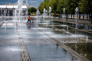 Su fıskiyelerinin arasında scooter süren küçük bir çocuk.
