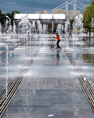 Su fıskiyelerinin arasında scooter süren küçük bir çocuk.