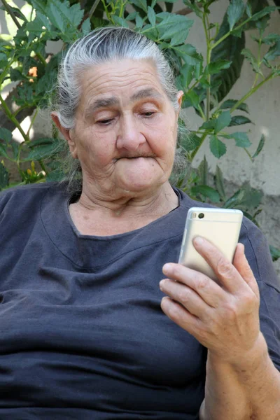 Old woman looking on a smartphone with curiosity