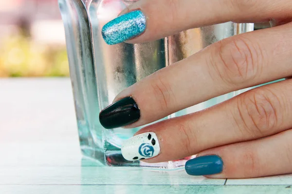 female hand with painted colorfull nails holds a glass of water on the table