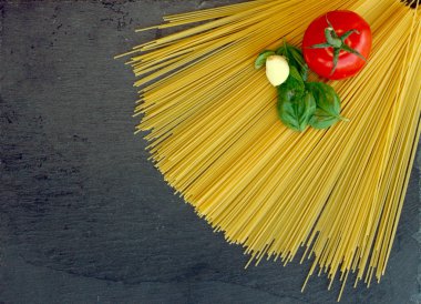 Pişmemiş makarna domates fesleğen ve kara tahta yukarıdan sarımsak ile