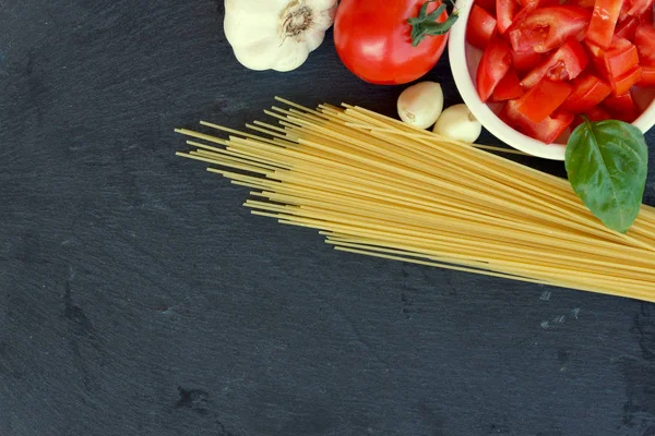 Spaghetti crudi con pomodoro baslil e aglio su lavagna nera Foto Stock