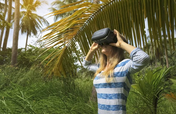 Virtual reality VR 3D headset and woman exploring the play on a background of nature jungle