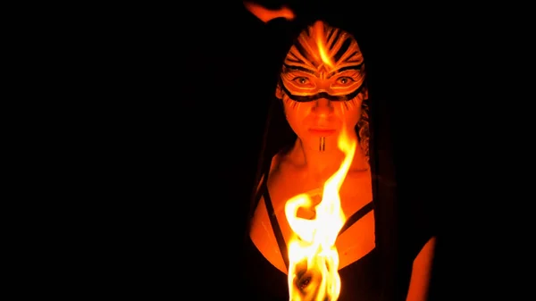 Woman with painted face posing with fire burning staff