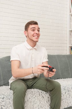 Bir genç bir uzaktan kumanda ile kanepede oturuyor ve Tv izliyor