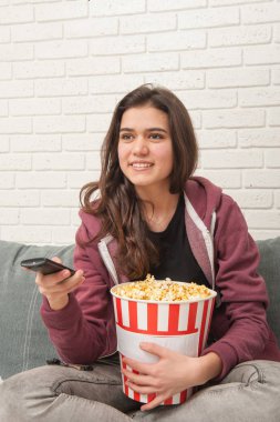 Tv Uzaktan ile kanepede oturan ve patlamış mısır yemek Genç kız