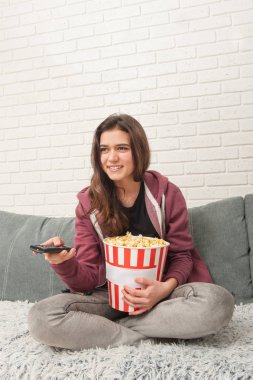 Tv Uzaktan ile kanepede oturan ve patlamış mısır yemek Genç kız
