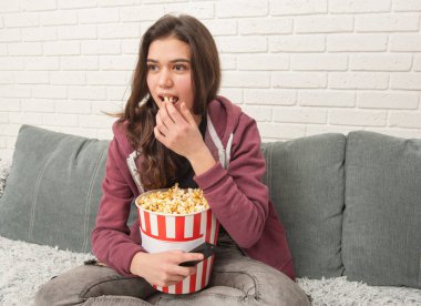 Tv Uzaktan ile kanepede oturan ve patlamış mısır yemek Genç kız