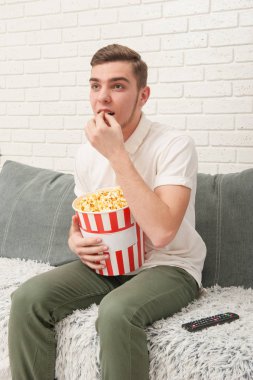 Bir genç çocuk TV izliyor ve patlamış mısır yemek