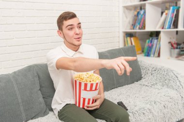 Bir genç çocuk TV izliyor ve patlamış mısır yemek