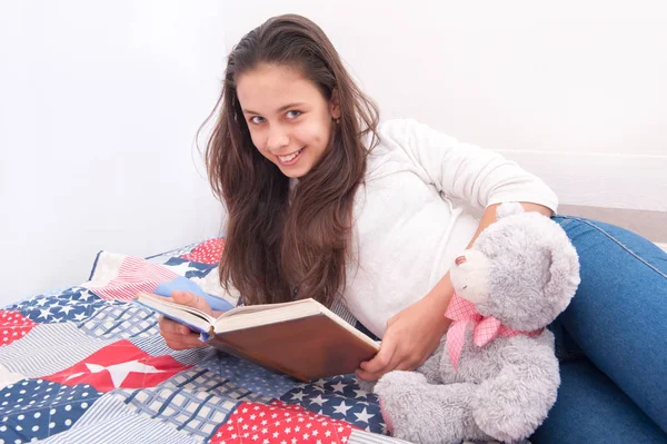 Chica está acostada en la cama y leyendo un libro — Foto de Stock