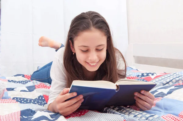 Chica está acostada en la cama y leyendo un libro — Foto de Stock