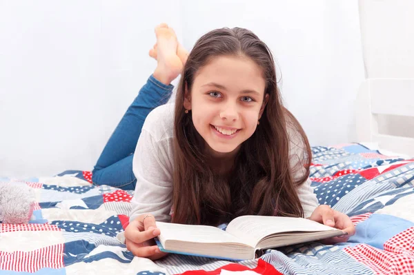 Chica está acostada en la cama y leyendo un libro — Foto de Stock