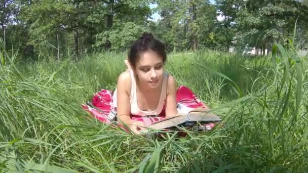 Dziewczyna czyta latem książkę na łące. — Wideo stockowe