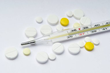 Beyaz arka planda termometre ve çok renkli haplar