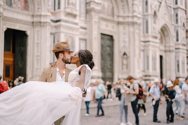 Multiraciaal echtpaar. Bruiloft in Florence, Italië. Kaukasische bruidegom cirkels en kussen Afro-Amerikaanse bruid op Piazza del Duomo. — Stockfoto