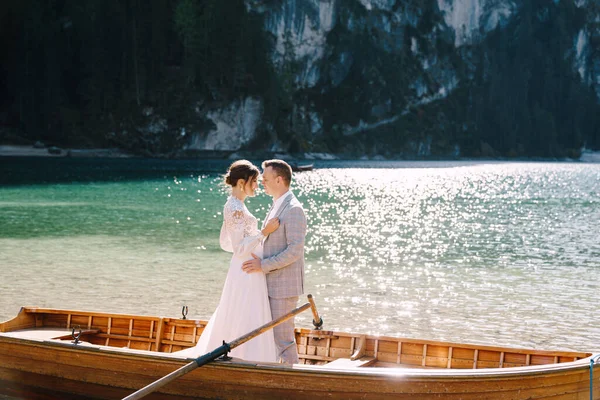 Menyasszony és vőlegény vitorlázás fa hajó, evezők Lago di Braies tó Olaszországban. Esküvő Európában - A friss házasok egy csónakban ölelkeznek. — Stock Fotó