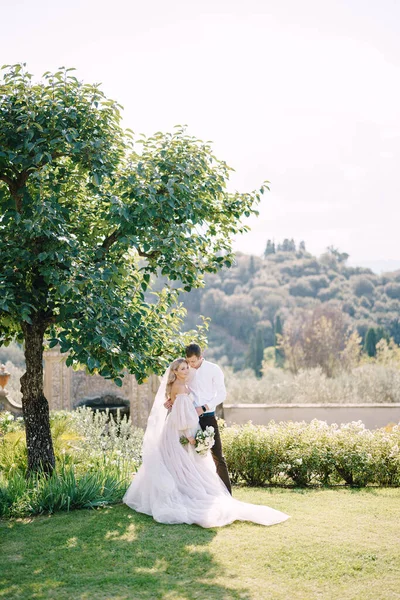 Esküvő Firenzében, Olaszországban, egy régi villa-pincészetben. Menyasszony és vőlegény egy fa árnyékában. Esküvői pár sétál a kertben. — Stock Fotó
