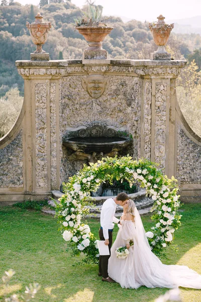 Besos de pareja de boda. Boda en una antigua villa bodega en Toscana, Italia. Arco de boda redondo decorado con flores blancas y vegetación frente a una antigua arquitectura italiana . —  Fotos de Stock