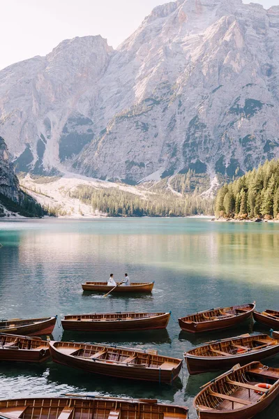 Pasangan pernikahan berlayar dengan perahu kayu di Lago di Braies, Italia. Pengantin baru di Eropa, di danau Braies, di Dolomites. Pengantin pria mendayung dayung, mempelai wanita duduk di depannya. Stok Gambar Bebas Royalti