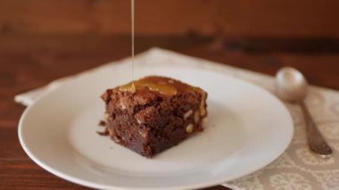 Kare dilim çikolatalı brownie tabakta, ahşap bir arka planda peçete ve kaşıkla yapışkan tuzlu karamelli