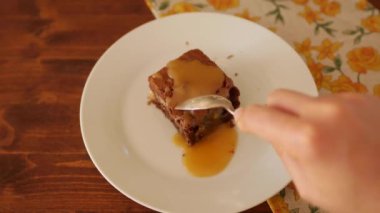 Kadının elindeki kaşık, Kare Çikolatalı Brownie 'nin parçalarını bir tabakta kırıyor. Kız pastayı yer, birinci şahıs manzarası, üst manzara....