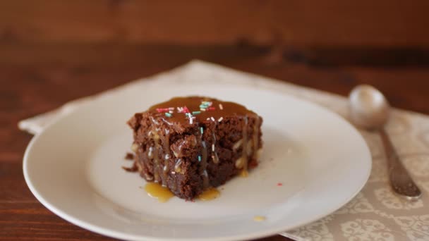 Een vierkant stukje Chocolade Brownie op een bord bestrooid met veelkleurig banketbakkerspoeder. — Stockvideo