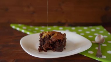 Tabağa bir parça çikolatalı Brownie. Tuzlu karamel dökülmüş. Beyaz noktalı yeşil bir peçete ve gümüş bir kaşık. 