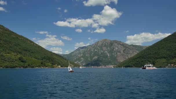 Tivat, Чорногорія - 15 травня 2016: Regatta - вітрильні яхти на морі, Чорногорія, Которська затока. Невелика вітрильна яхта плаває на тлі зелених гір, блакитного неба з хмарами і. Пором для пасажирів. — стокове відео