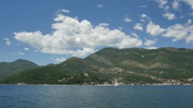 Tivat, Karadağ - 15 Mayıs 2016: Karadağ, Kotor Körfezi 'ndeki yat yarışları. Kamenari şehrinin arka planında küçük yelkenli yatı, yeşil bahar dağları, beyaz bulutlu mavi gökyüzü