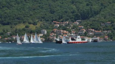 Tivat, Karadağ - 15 Mayıs 2016: Karadağ 'ın Kotor Körfezi' ndeki bir feribot küçük yelkenli yatlardan geçiyor. Yelkenli teknelerde spor yarışı, deniz yarışları..