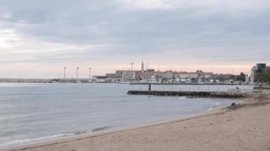 Budva 'daki tekne ve yatlar için rıhtım, eski kasabanın yakınında. Kasvetli bulutlu sonbahar gökyüzü. Şehrin üzerinde kurşun bulutlar asılı. Rıhtımdaki balıkçı..